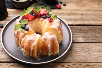 Photo of Pieces of delicious bundt cake with berries, glaze and mint on wooden table, closeup