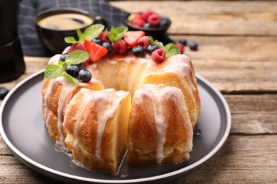 Photo of Pieces of delicious bundt cake with berries, glaze and mint on wooden table, closeup