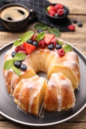 Photo of Pieces of delicious bundt cake with berries, glaze and mint on wooden table, closeup
