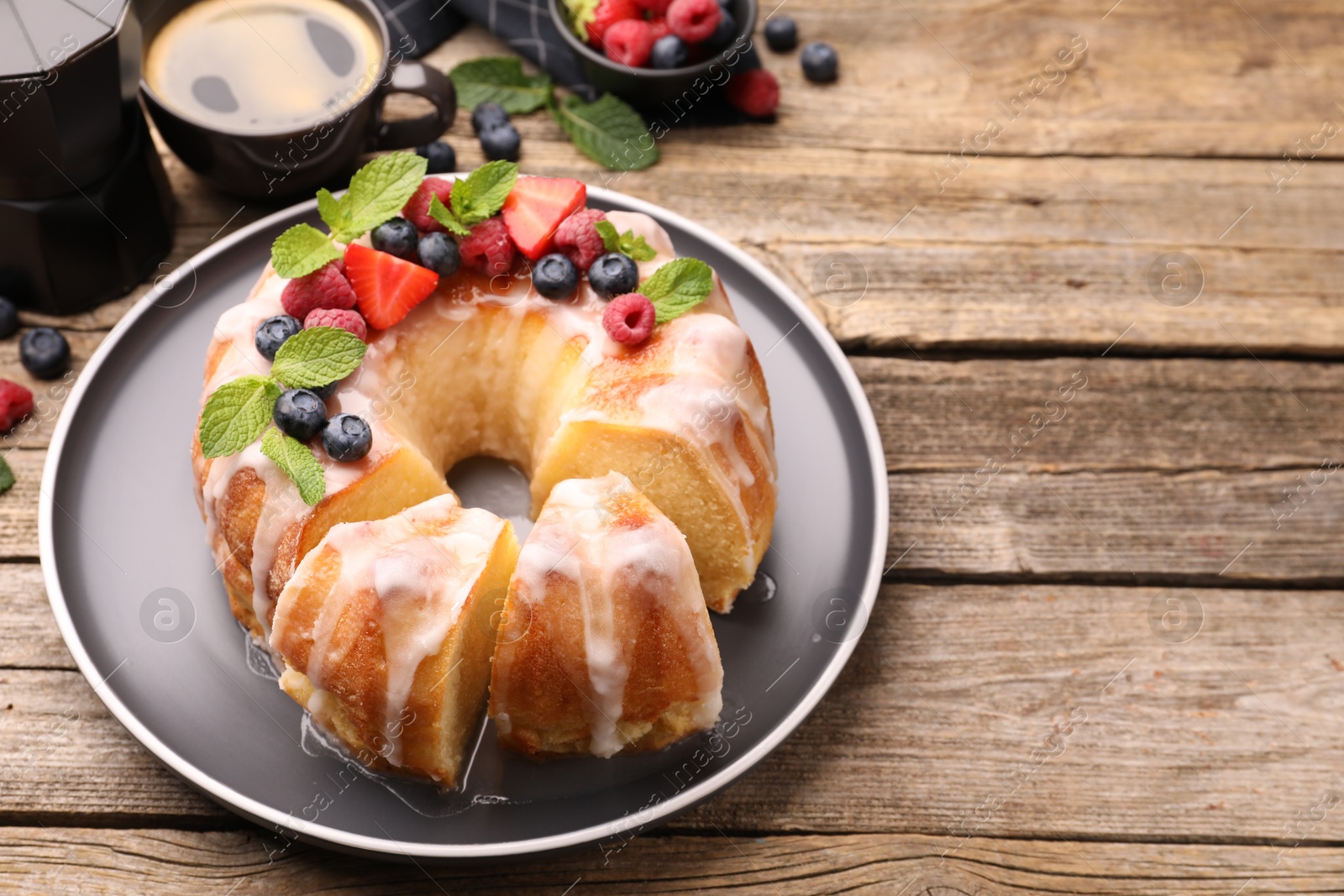Photo of Pieces of delicious bundt cake with berries, glaze and mint on wooden table, closeup