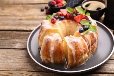 Photo of Pieces of delicious bundt cake with berries, glaze and mint on wooden table, closeup