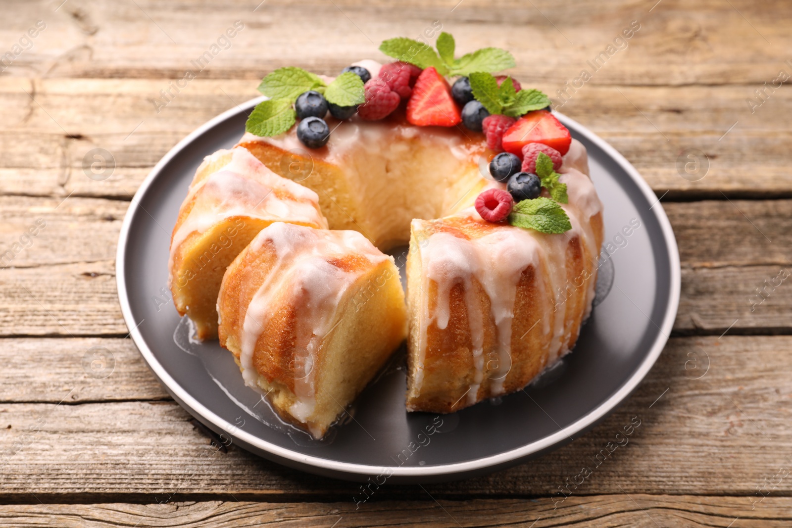 Photo of Pieces of delicious bundt cake with berries, glaze and mint on wooden table, closeup