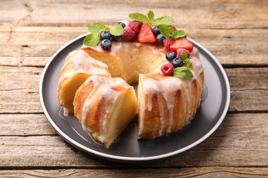 Photo of Pieces of delicious bundt cake with berries, glaze and mint on wooden table, closeup