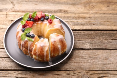 Photo of Pieces of delicious bundt cake with berries, glaze and mint on wooden table, closeup