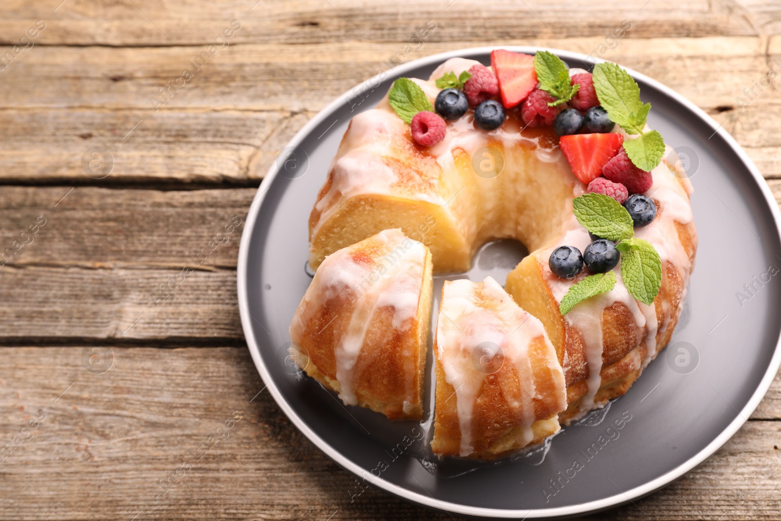 Photo of Pieces of delicious bundt cake with berries, glaze and mint on wooden table, closeup