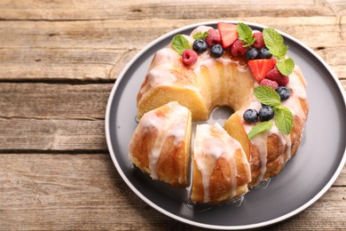 Photo of Pieces of delicious bundt cake with berries, glaze and mint on wooden table, closeup