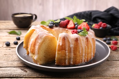 Photo of Pieces of delicious bundt cake with berries, glaze and mint on wooden table, closeup
