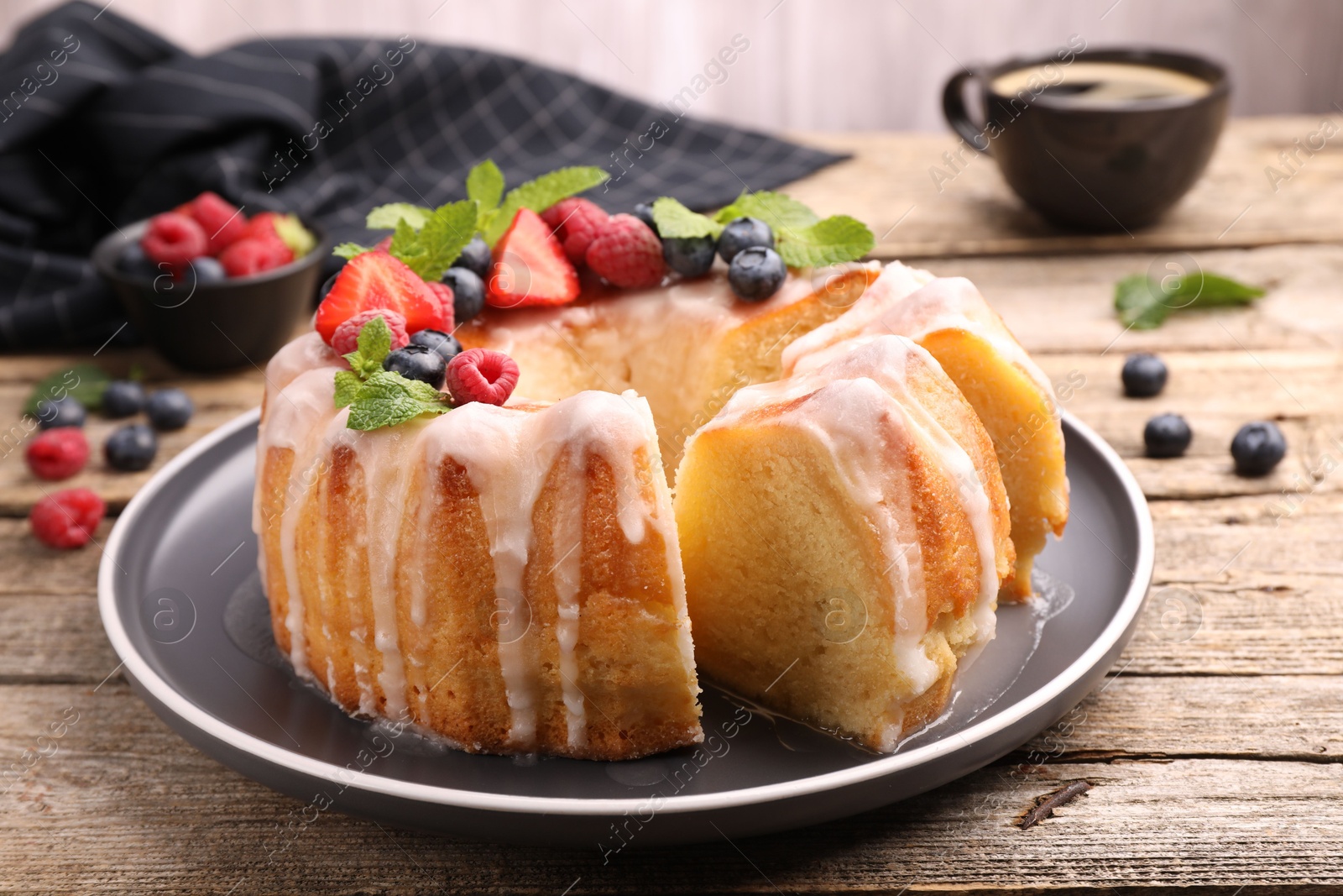 Photo of Pieces of delicious bundt cake with berries, glaze and mint on wooden table, closeup