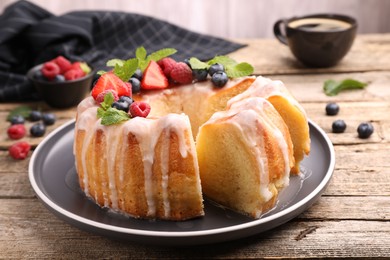 Photo of Pieces of delicious bundt cake with berries, glaze and mint on wooden table, closeup