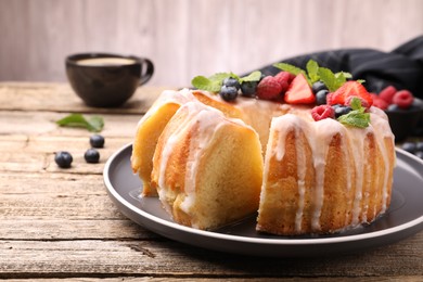 Photo of Pieces of delicious bundt cake with berries, glaze and mint on wooden table, closeup