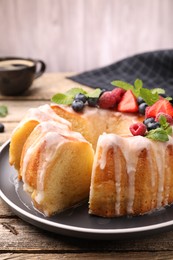 Photo of Pieces of delicious bundt cake with berries, glaze and mint on wooden table, closeup