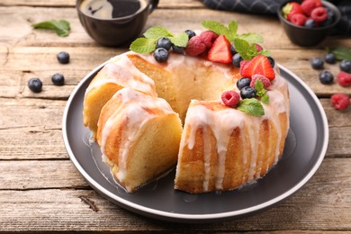 Photo of Pieces of delicious bundt cake with berries, glaze and mint on wooden table, closeup