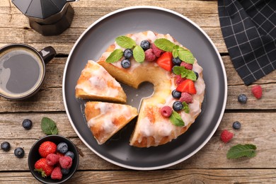 Photo of Pieces of delicious bundt cake with berries, glaze and mint on wooden table, flat lay