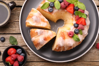 Photo of Pieces of delicious bundt cake with berries, glaze and mint on wooden table, flat lay