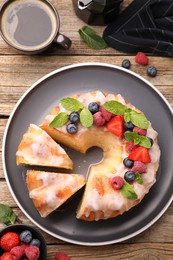 Photo of Pieces of delicious bundt cake with berries, glaze and mint on wooden table, flat lay