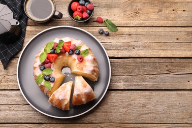 Photo of Pieces of delicious bundt cake with berries, glaze and mint on wooden table, flat lay. Space for text