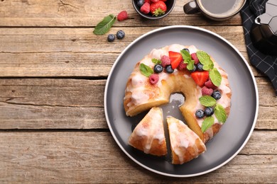 Photo of Pieces of delicious bundt cake with berries, glaze and mint on wooden table, flat lay. Space for text