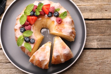 Photo of Pieces of delicious bundt cake with berries, glaze and mint on wooden table, top view