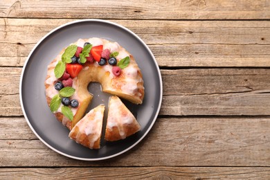 Photo of Pieces of delicious bundt cake with berries, glaze and mint on wooden table, top view. Space for text
