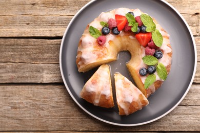 Photo of Pieces of delicious bundt cake with berries, glaze and mint on wooden table, top view