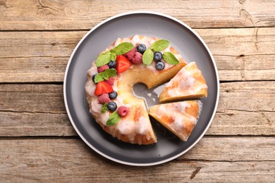 Photo of Pieces of delicious bundt cake with berries, glaze and mint on wooden table, top view