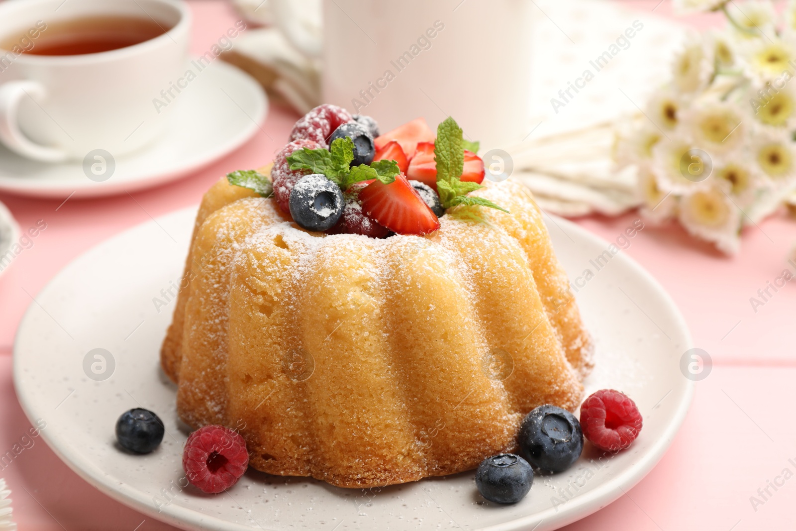 Photo of Delicious bundt cake with powdered sugar, berries and mint on pink wooden table, closeup