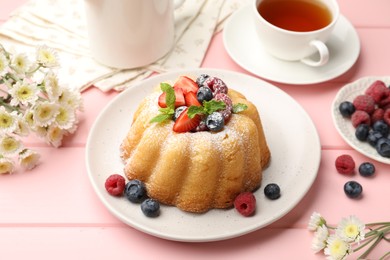 Photo of Delicious bundt cake with powdered sugar, berries and mint on pink wooden table, closeup