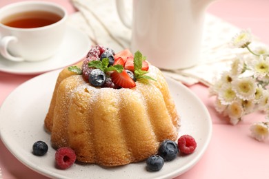 Photo of Delicious bundt cake with powdered sugar, berries and mint on pink wooden table, closeup