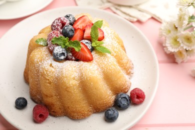 Photo of Delicious bundt cake with powdered sugar, berries and mint on pink wooden table, closeup