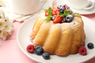 Photo of Delicious bundt cake with powdered sugar, berries and mint on pink wooden table, closeup