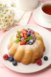 Photo of Delicious bundt cake with powdered sugar, berries and mint on pink wooden table, closeup