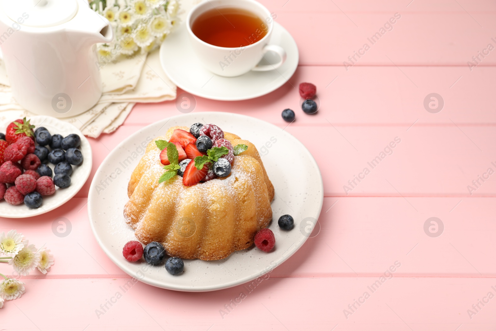Photo of Delicious bundt cake with powdered sugar, berries, mint and tea on pink wooden table