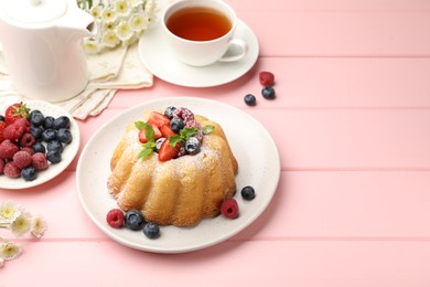 Photo of Delicious bundt cake with powdered sugar, berries, mint and tea on pink wooden table