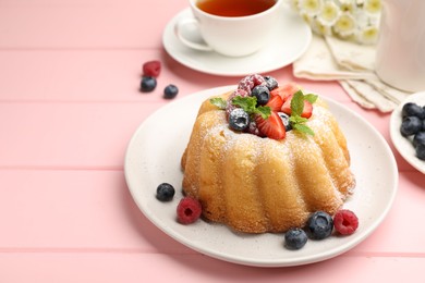 Photo of Delicious bundt cake with powdered sugar, berries and mint on pink wooden table, closeup