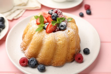 Photo of Delicious bundt cake with powdered sugar, berries and mint on pink wooden table, closeup