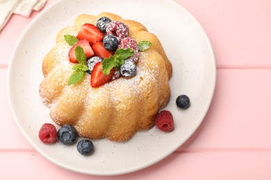 Photo of Delicious bundt cake with powdered sugar, berries and mint on pink wooden table, closeup