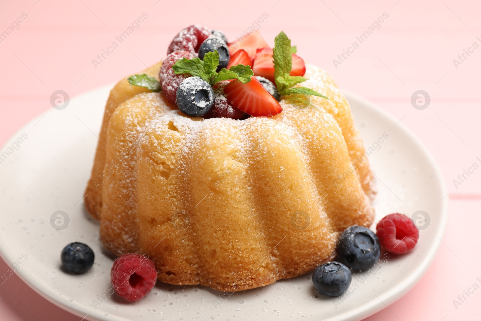 Photo of Delicious bundt cake with powdered sugar, berries and mint on pink table, closeup