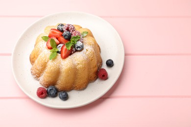 Photo of Delicious bundt cake with powdered sugar, berries and mint on pink wooden table