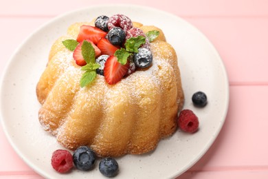 Photo of Delicious bundt cake with powdered sugar, berries and mint on pink wooden table, closeup