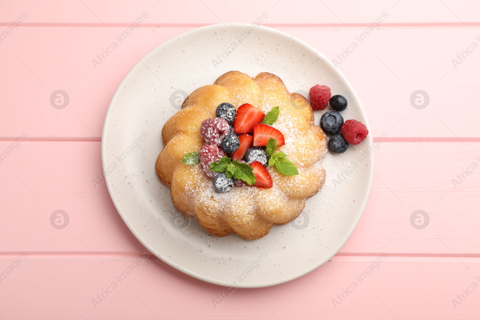 Photo of Delicious bundt cake with powdered sugar, berries and mint on pink wooden table, top view