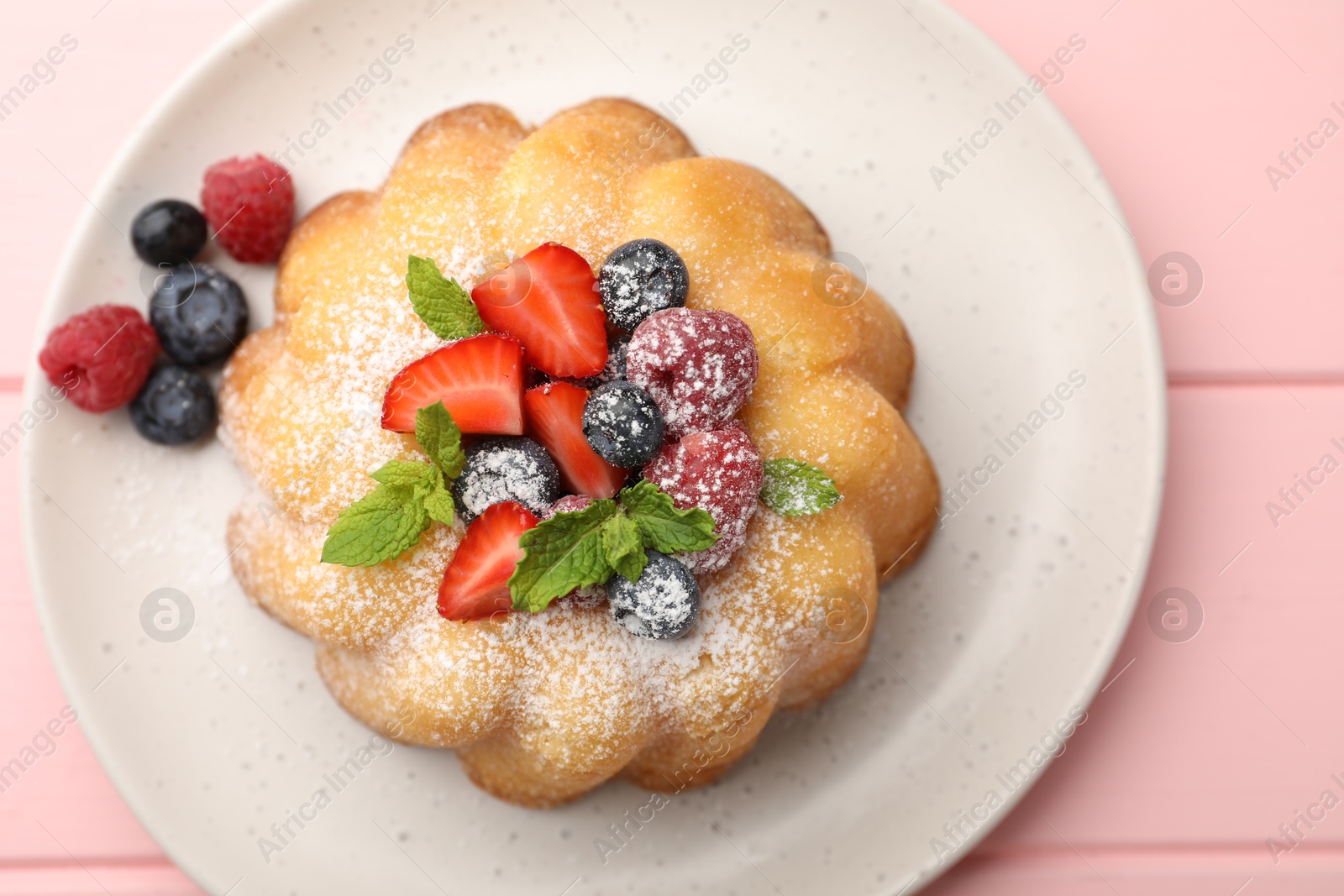 Photo of Delicious bundt cake with powdered sugar, berries and mint on pink wooden table, top view