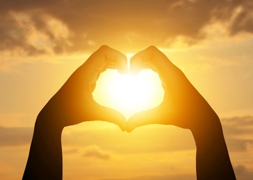 Image of Hope. Sun shining through heart made of woman's hands against sunrise sky, closeup