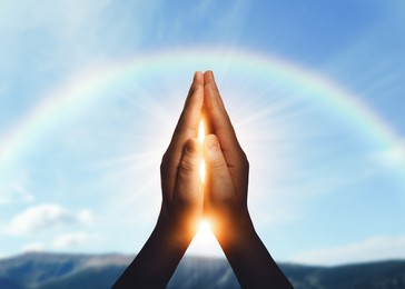 Image of Hope. Man holding hands against sky with rainbow and sun, closeup