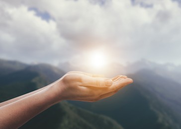 Image of Hope. Woman holding hands against sky with clouds and sun in mountains, closeup