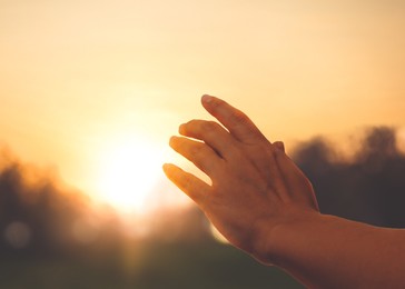 Image of Hope. Woman reaching out her hand toward sun outdoors, closeup