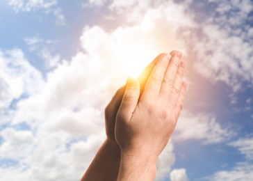 Image of Hope. Man praying and holding hands against sky with sun and clouds, closeup