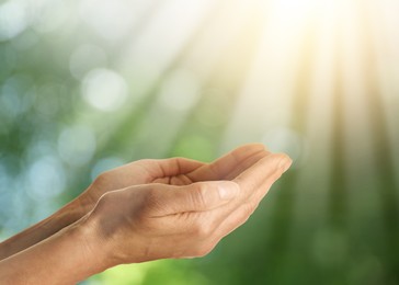 Image of Hope. Woman holding hands against blurred green background with light, closeup