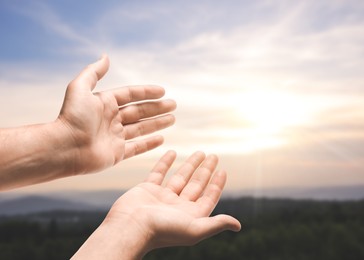 Image of Hope. Man holding hands against sky with clouds and sun in mountains, closeup