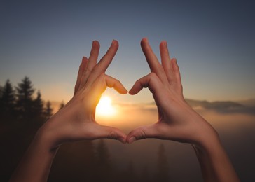 Image of Hope. Woman making heart with hands against sun in mountains, closeup