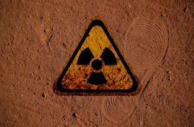 Image of Radioactive sign on brown ground with shoes track, top view. Radiological pollution